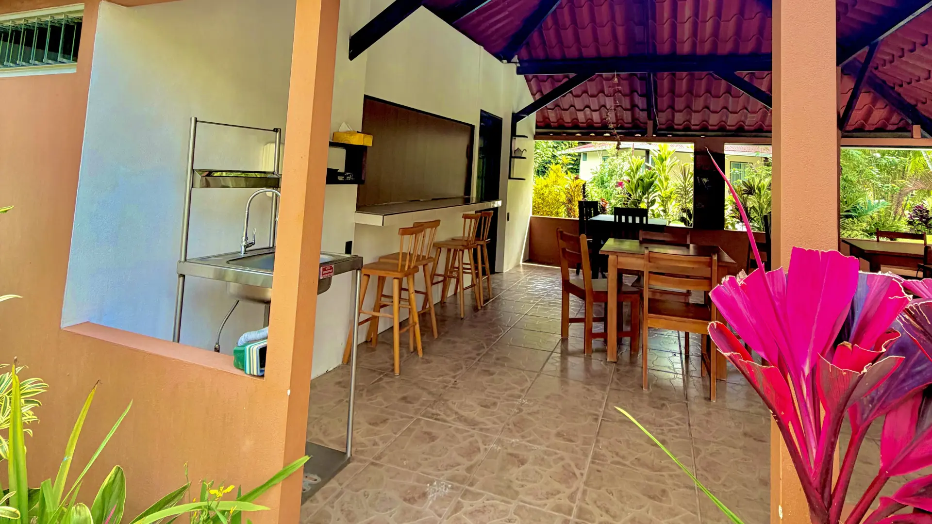 Comedor techado para desayunos con mesas de madera, barra con taburetes y vista a jardines tropicales en La Fortuna.