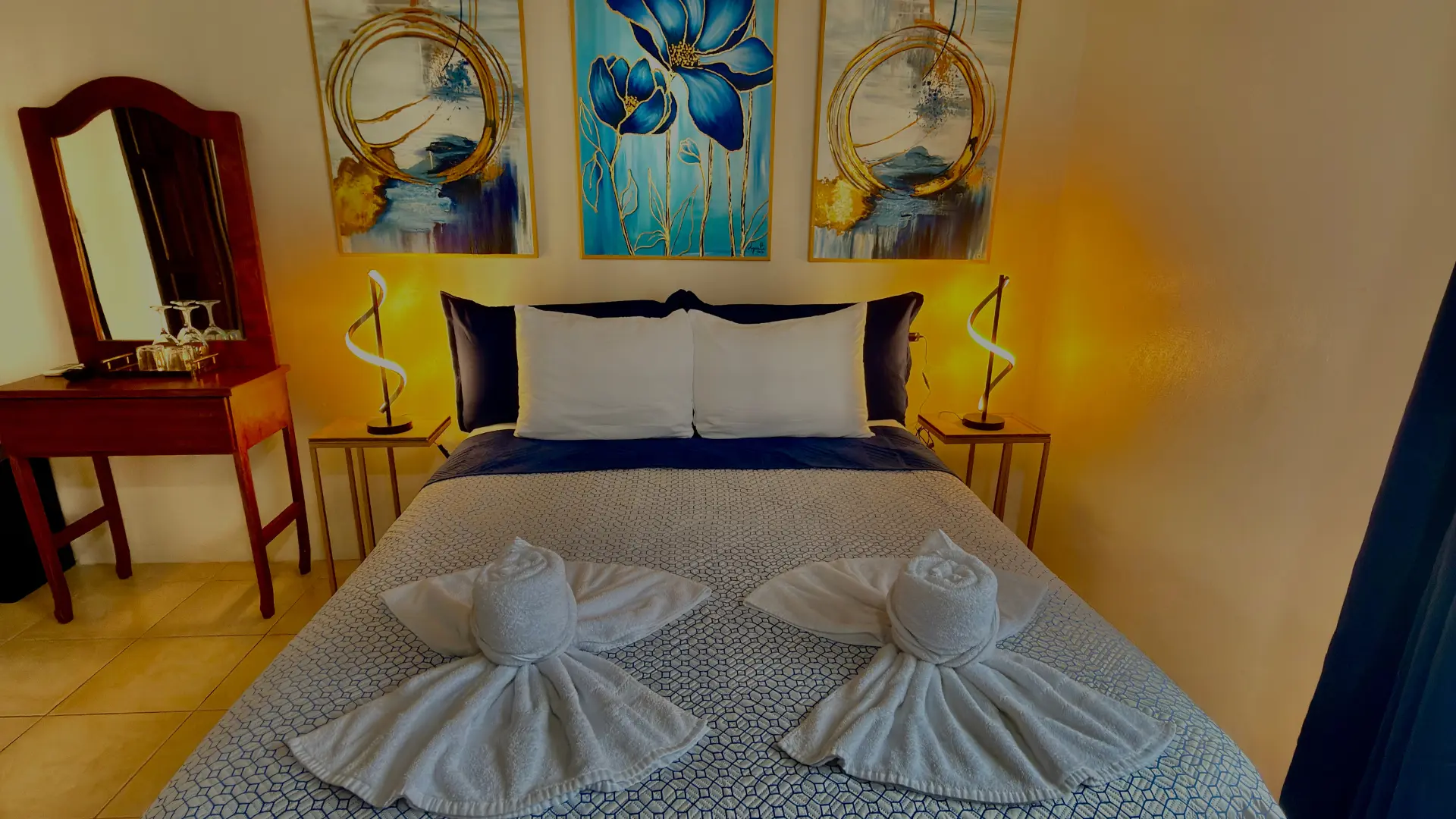 Cama matrimonial con decoración de cisnes con toallas y lámparas modernas en habitación de Loma Real Hotel.